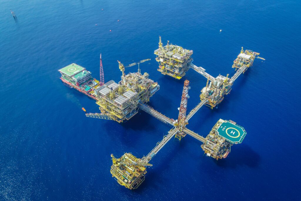 pexels-photo-9336590-9336590 Drone shot of a large, complex offshore oil platform in deep blue ocean waters.
